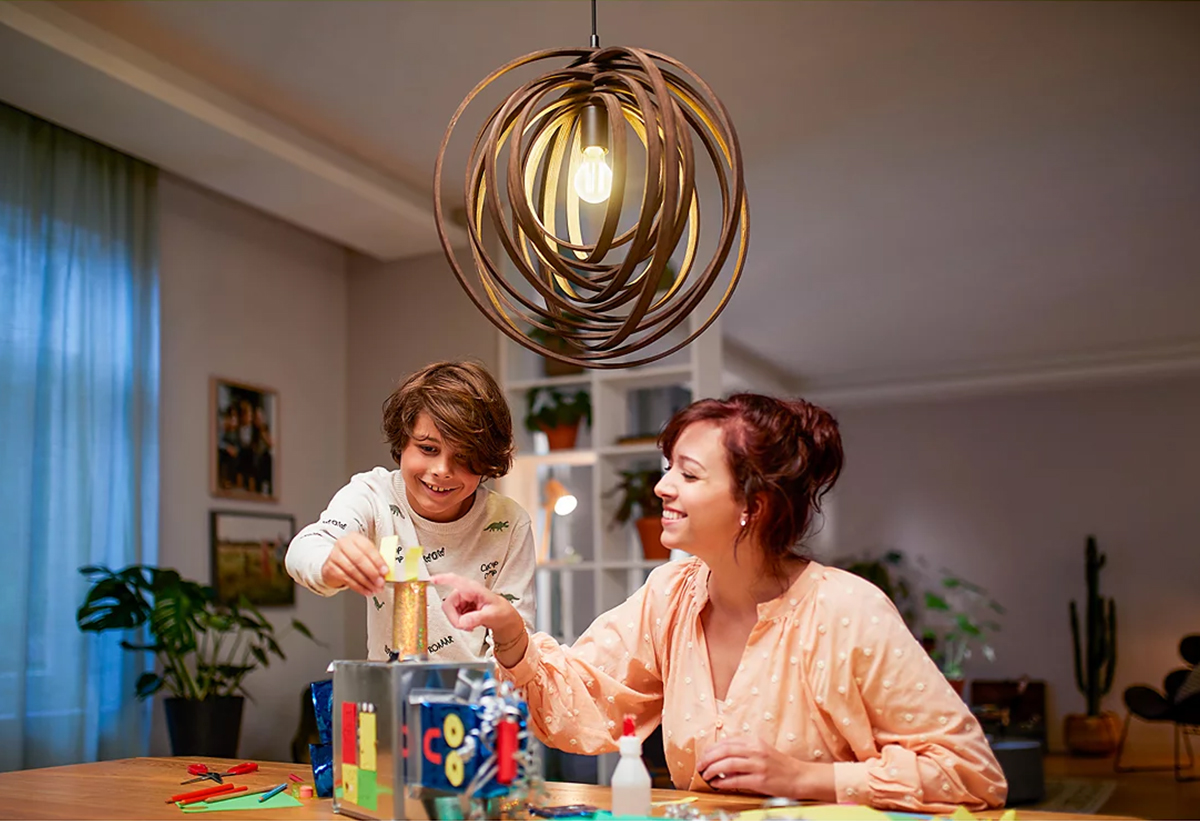 Μία μαμά με τον παιδί της παίζουν στο σαλόνι με επαρκή φωτισμό από το φωτιστικό με την λάμπα Philips ακριβώς από πάνω τους